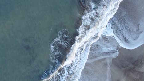 Amazing-aerial-shot-of-the-sea-waves-breaking-on-the-shore-in-Cariló,-Argentina