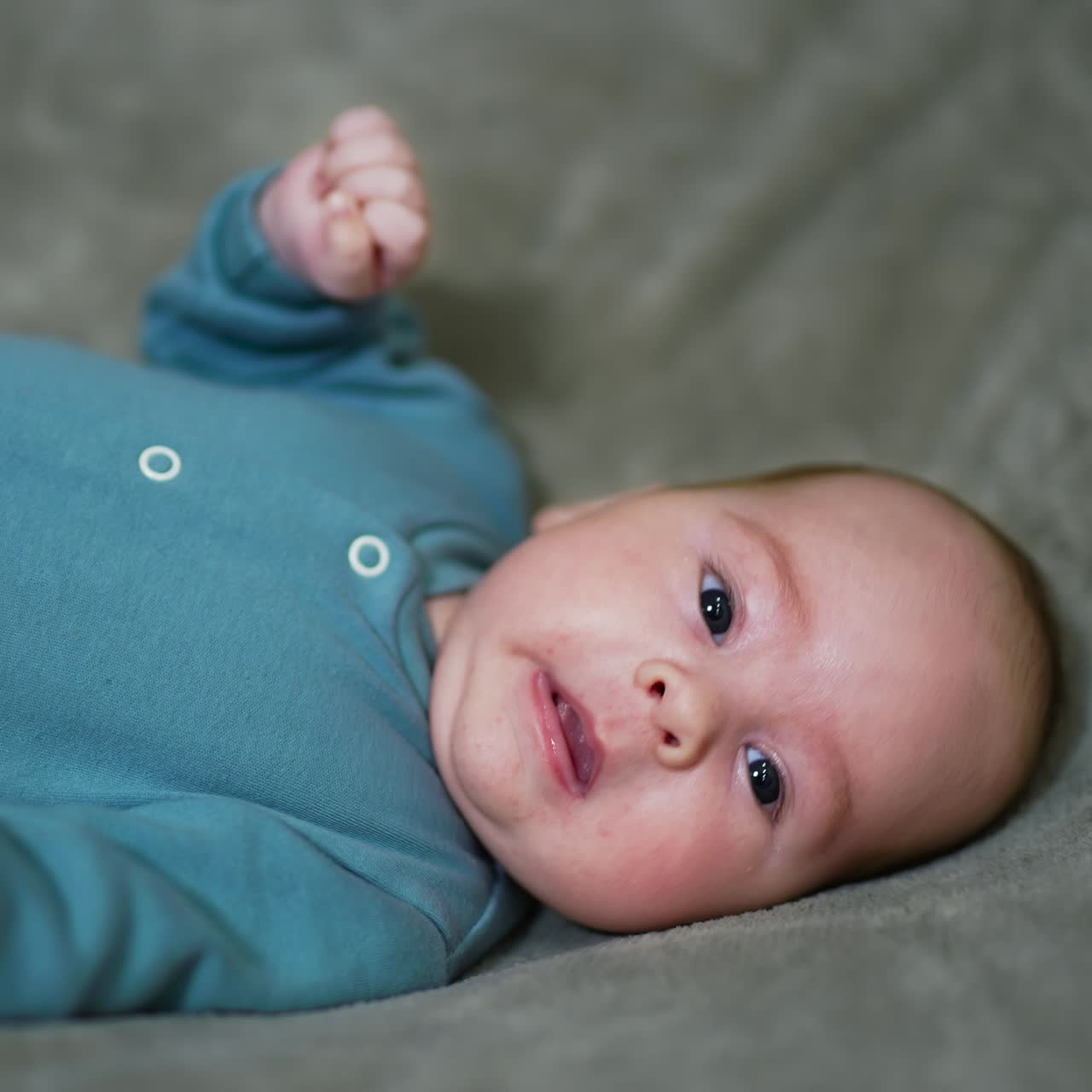 Funny baby on the bed with his head turned right. Beautiful baby looks into camera and sneezes. Gray backdrop