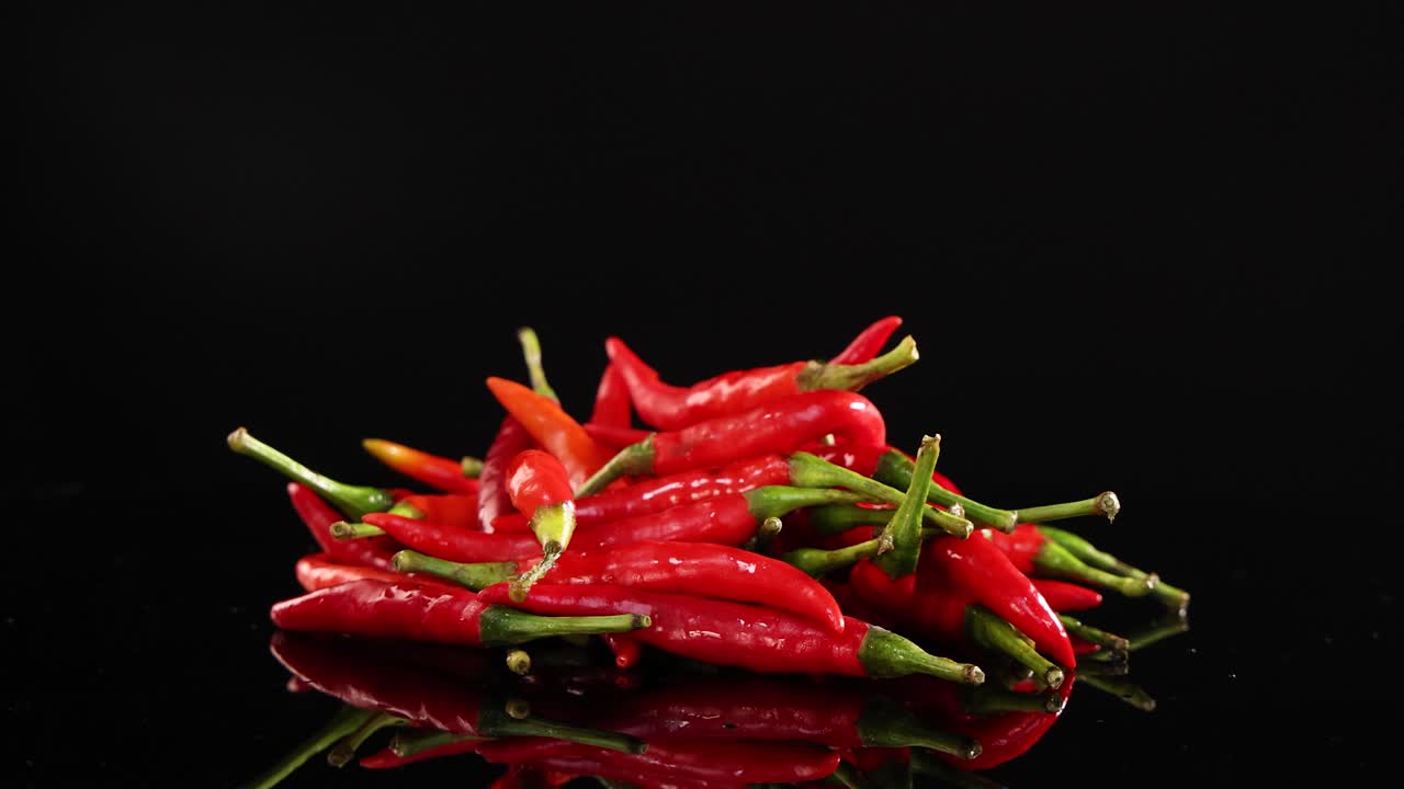 A pile of red chili peppers rotates on a reflective black surface under bright lighting