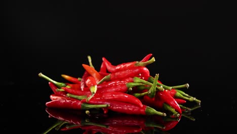 a pile of red chili peppers rotates on a reflective black surface under bright lighting