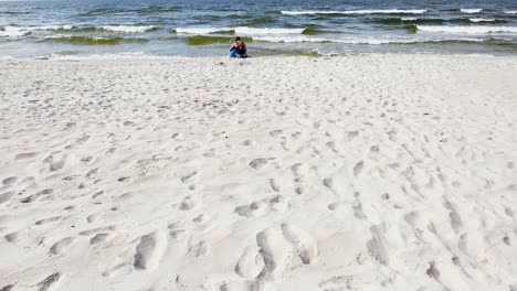 a mother and child sitting on beautiful white sandy shore of baltic sea with waves splashing on a sunny day