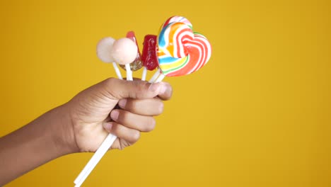 hand holding lollipop candy on yellow background