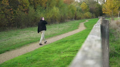 man on phone call walks down dirt path in a park away from camera