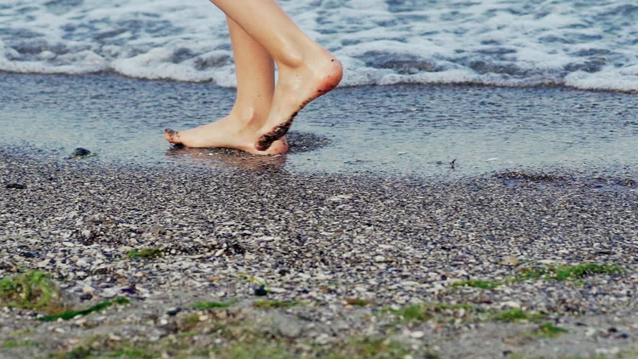 Female legs close up. Woman walking on beach barefoot at sunset. Slow motion.