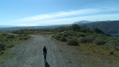 drone flying towards the ocean, capturing a woman running in the mountains