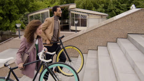 Vista-Lateral-De-Un-Hombre-Y-Una-Mujer-Americanos-Con-Ropa-Formal-Llevando-Sus-Bicicletas-Por-Las-Escaleras-Mientras-Van-Al-Trabajo
