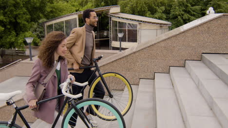 vista lateral de un hombre y una mujer americanos con ropa formal llevando sus bicicletas por las escaleras mientras van al trabajo