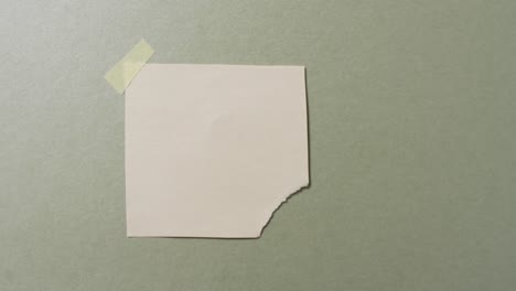 Video-of-close-up-of-torn-piece-of-white-paper-taped-on-green-background
