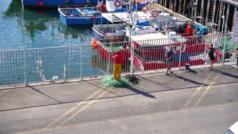 worker in bright yellow overalls gathers fishing nets by docked boats at santona port in cantabria