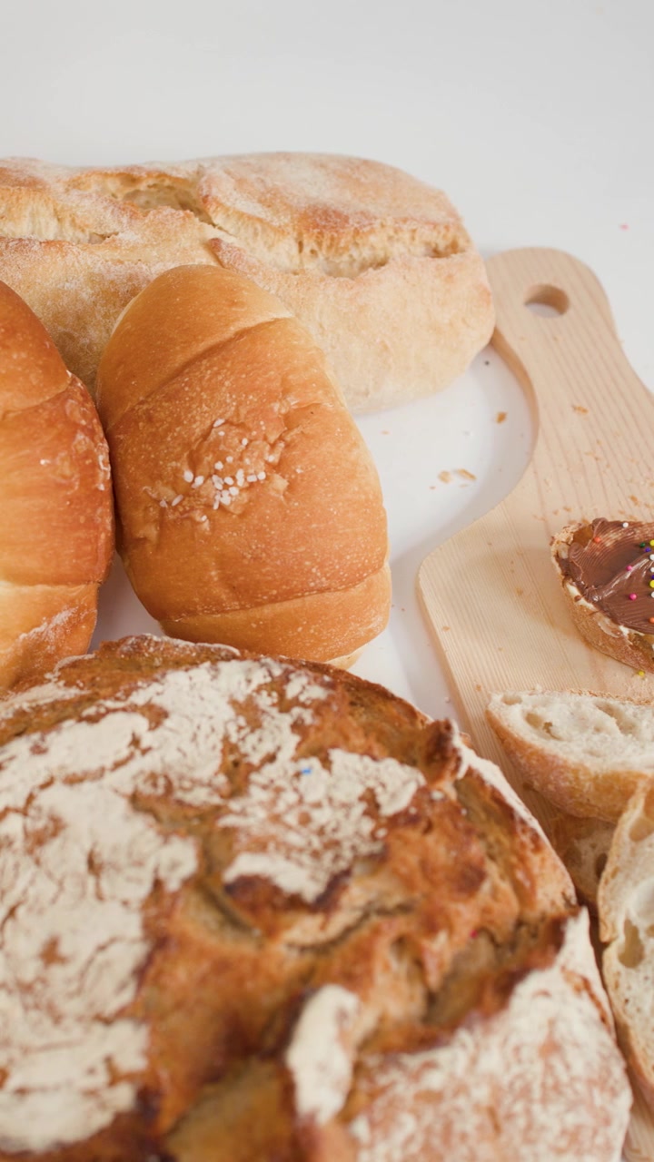 Top-down view of various breads and pastries while hand adds colorful sprinkles to chocolate spread.