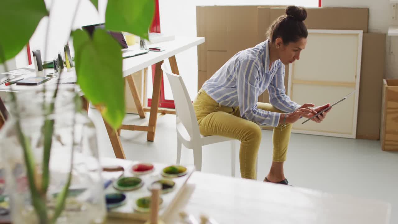 video de una feliz diseñadora biracial usando una tableta en el estudio