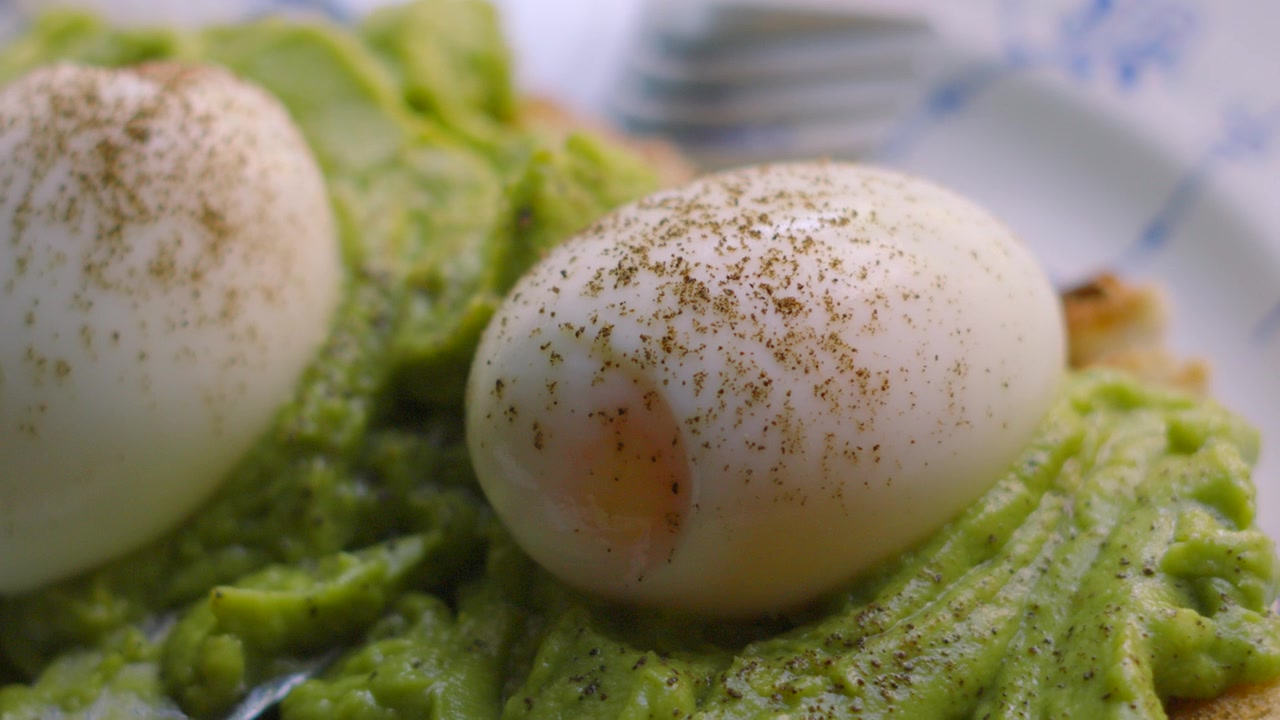 Gros plan sur des œufs à la coque frais avec du poivre et de l'avocat écrasé sur du pain au levain. Petit-déjeuner sain et faible en gras