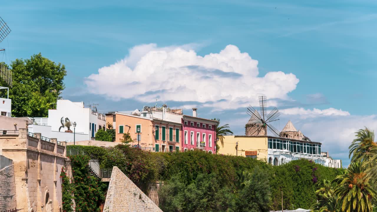 Timelapse of colorful houses
with distant storm clouds in Palma, Mallorca, Spain.
Traditional windmill and vibrant facades with lush greenery and blue skies. A charming island scene.