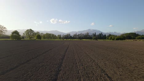 low drone flight over freshly plowed, brown field at sunset