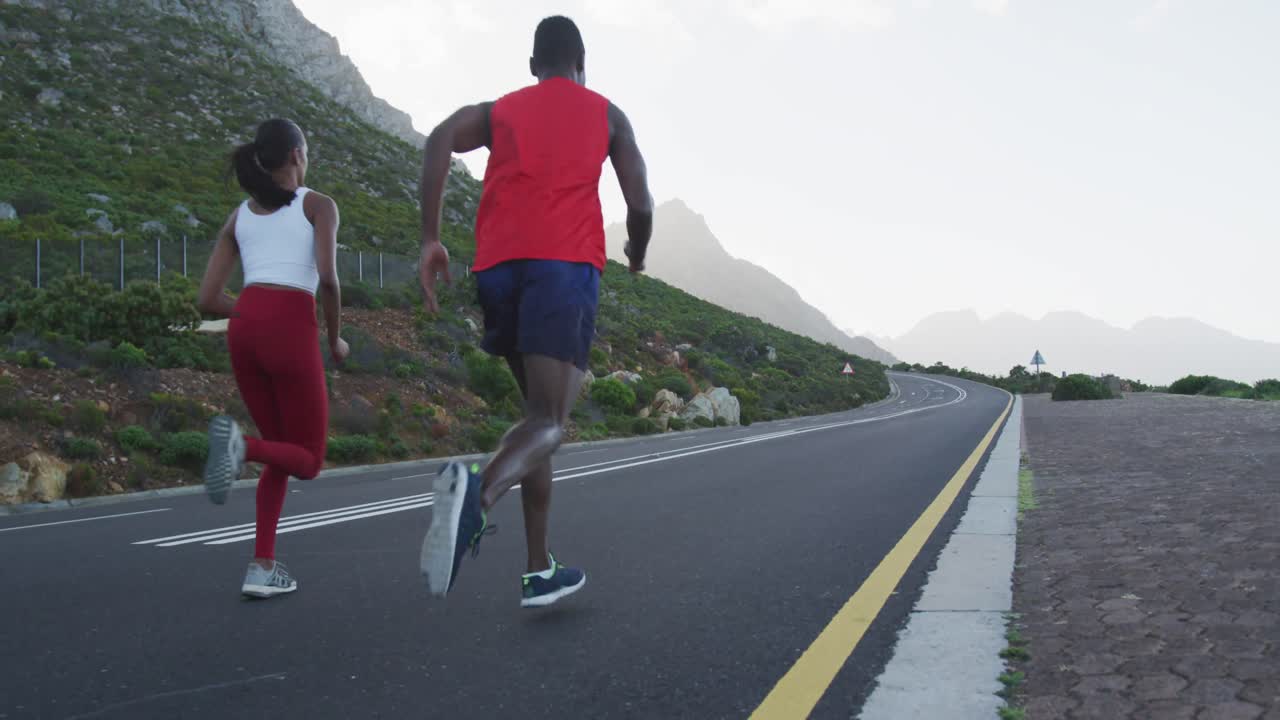 Diverse fit couple exercising running on a country road near mountains