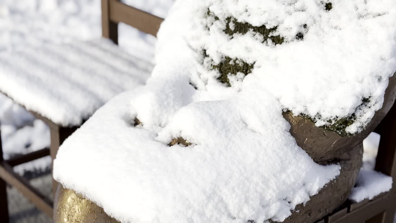 A poignant and cinematic shot of the 'Statue of Peace' (Sonyeosang), a bronze monument symbolizing the victims of wartime sexual slavery. The statue is covered in a fresh layer of white snow during a