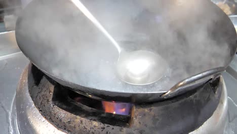 a cinematic slow-motion clip of a wok with boiling water over an open flame. steam rises dramatically, creating an intense and visually captivating scene of traditional asian cooking methods.