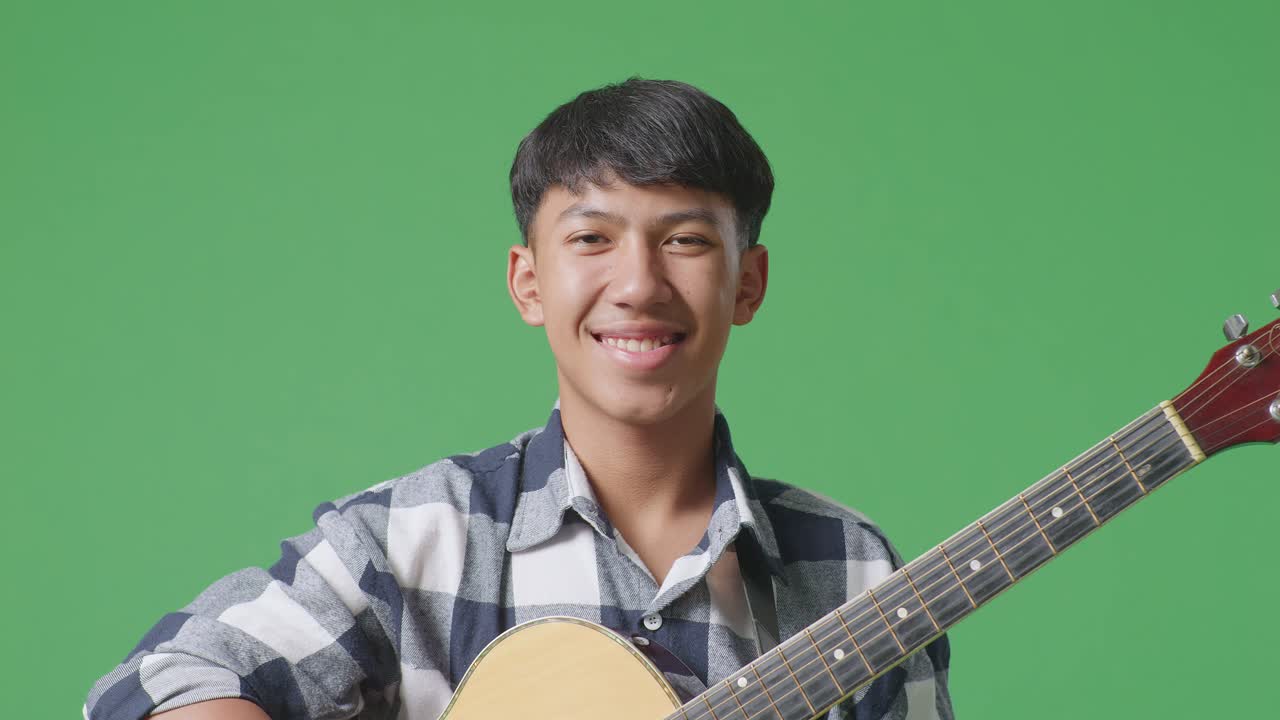 녹색 스크린 배경에 서 있는 동안 기타를 연주하는 아시아 십대 의 근접 사진