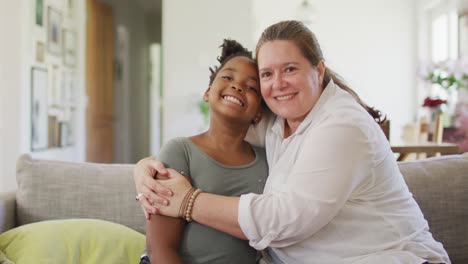 Portrait-of-happy-caucasian-woman-and-her-african-american-daughter-smiling-in-living-room