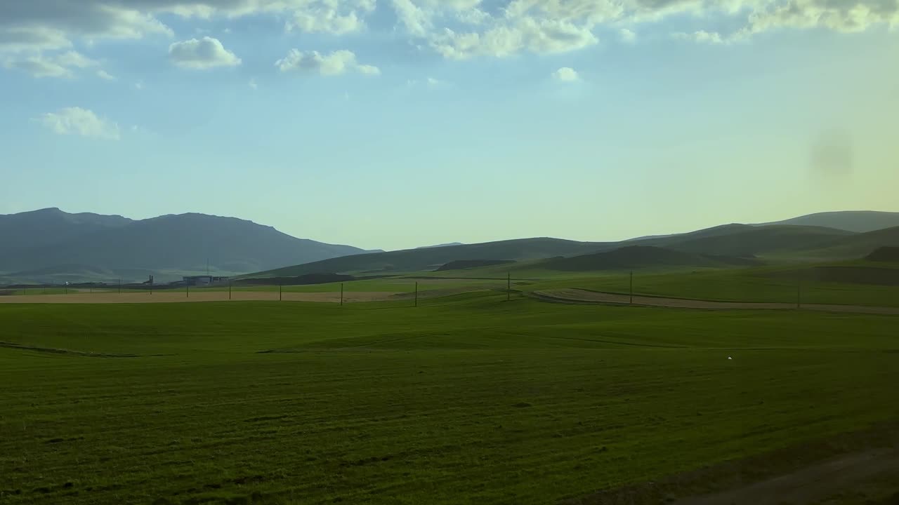 Naturskøn togrejse i Irans landskab med panoramaudsigt over bjerge, landbrugsmarker og frodig grøn natur i Kurdistan, set gennem et vindue i bevægelse – en rolig transitrejse.