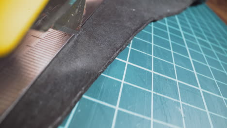 Person cuts black leather material with knife on table