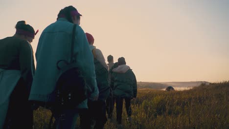 happy young people walk along grass field after day hike