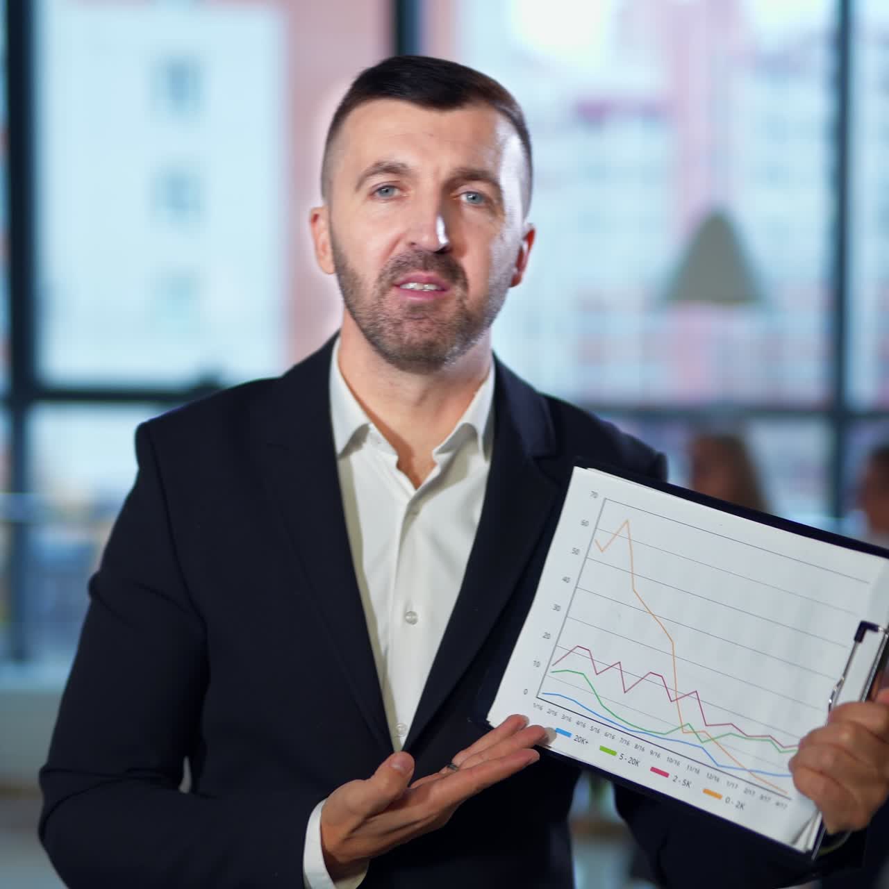 Businessman holding a flipchart with graphs and describing them. Bearded man speaking emotionally in front of camera. Close up portrait