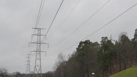 High-voltage-power-lines-running-through-green-park,-tilt,-Stockholm