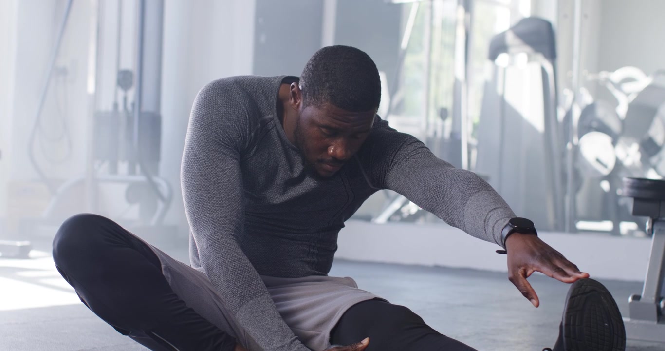 Man stretching leg on gym mat, reaching shoe, adjusting smartwatch, preparing workout