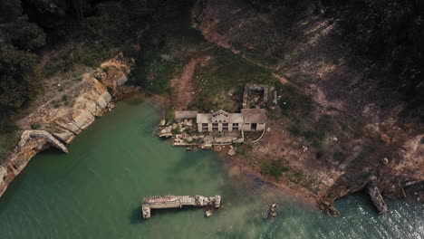 Unique-ascending-birdseye-view-shot-over-relics-on-a-river's-margin-at-São-Domingos-Dam,-Atouguia-da-Baleia,-Portugal