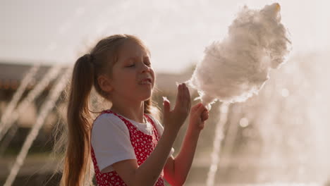 girl puts cotton candy in mouth and looks at sticky fingers