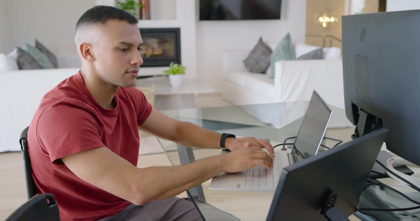 African American man at living-room desk, sitting, moving laptop, checking phone, typing, working