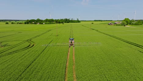 drone establishing shot shows tractor spraying crop field with turbines, latvia