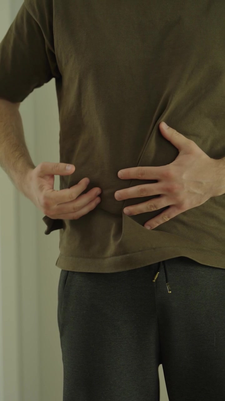 A man holds his stomach in pain, showing abdominal cramps, digestive problems, illness, discomfort, and health issues.