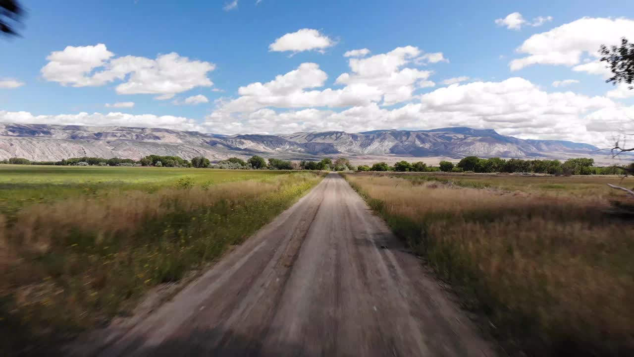 Dirt road through rural landscape with trees and mountains