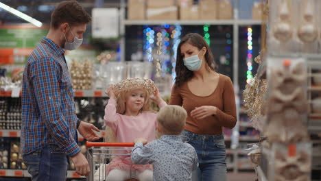 a married couple with two children in a shopping center in protective masks in the coronavirus epidemic are preparing for christmas and choosing decorations