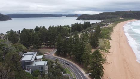 Drone-descending-over-a-peninsula-over-a-seaside-road-revealing-expensive-homes-built-on-a-cliff