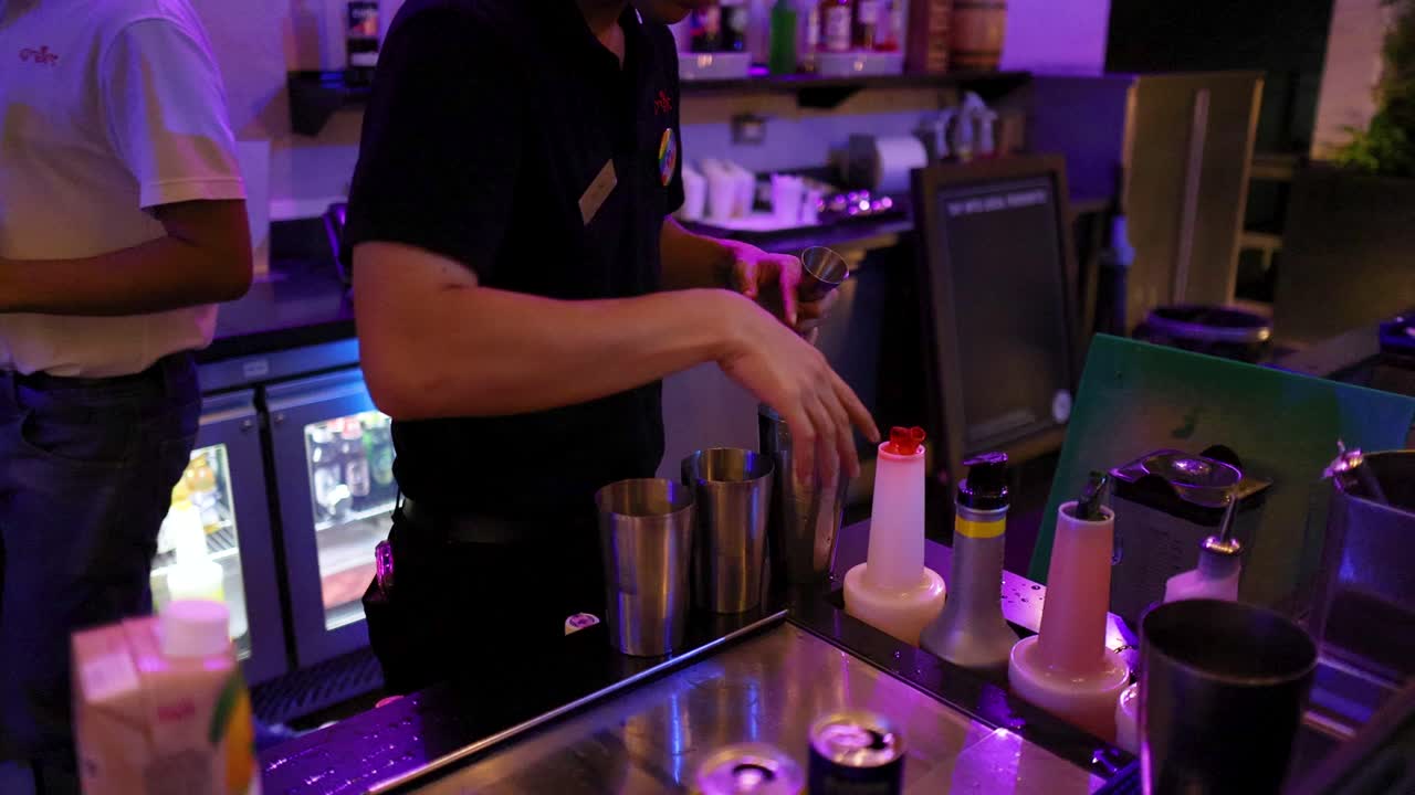 Bartender prepares ice cocktail at illuminated bar counter, using shaker and bottles, low-light ambiance