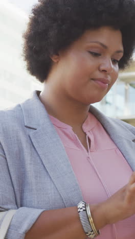 portrait of happy plus size biracial woman using smartphone in city