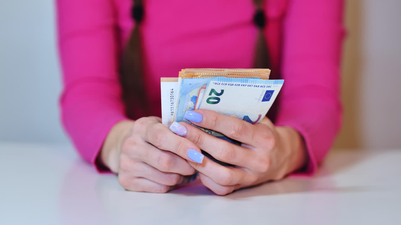Donna in rosa conta lentamente i contanti con calma e concentrazione, manifestando una mentalità di ricchezza