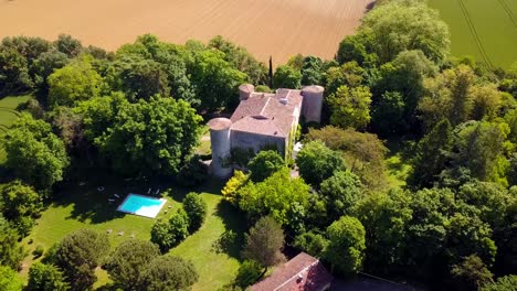 Vista-Aérea-De-Un-Castillo-Del-Sur-De-Francia-Con-Tres-Torres,-Piscina,-Bosques-Y-Campos-De-Trigo.