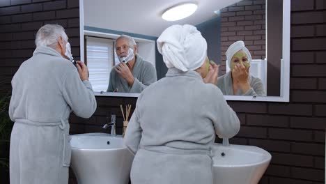 Old-senior-couple-man-and-woman-doing-morning-hygiene-procedures-and-looking-into-a-mirror