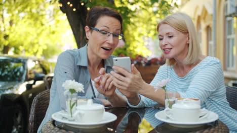 two women friends enjoying coffee and using smartphone