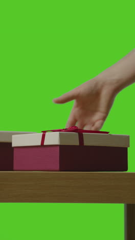 vertical video of man picking up presents in gift wrapped boxes from table shot against green screen