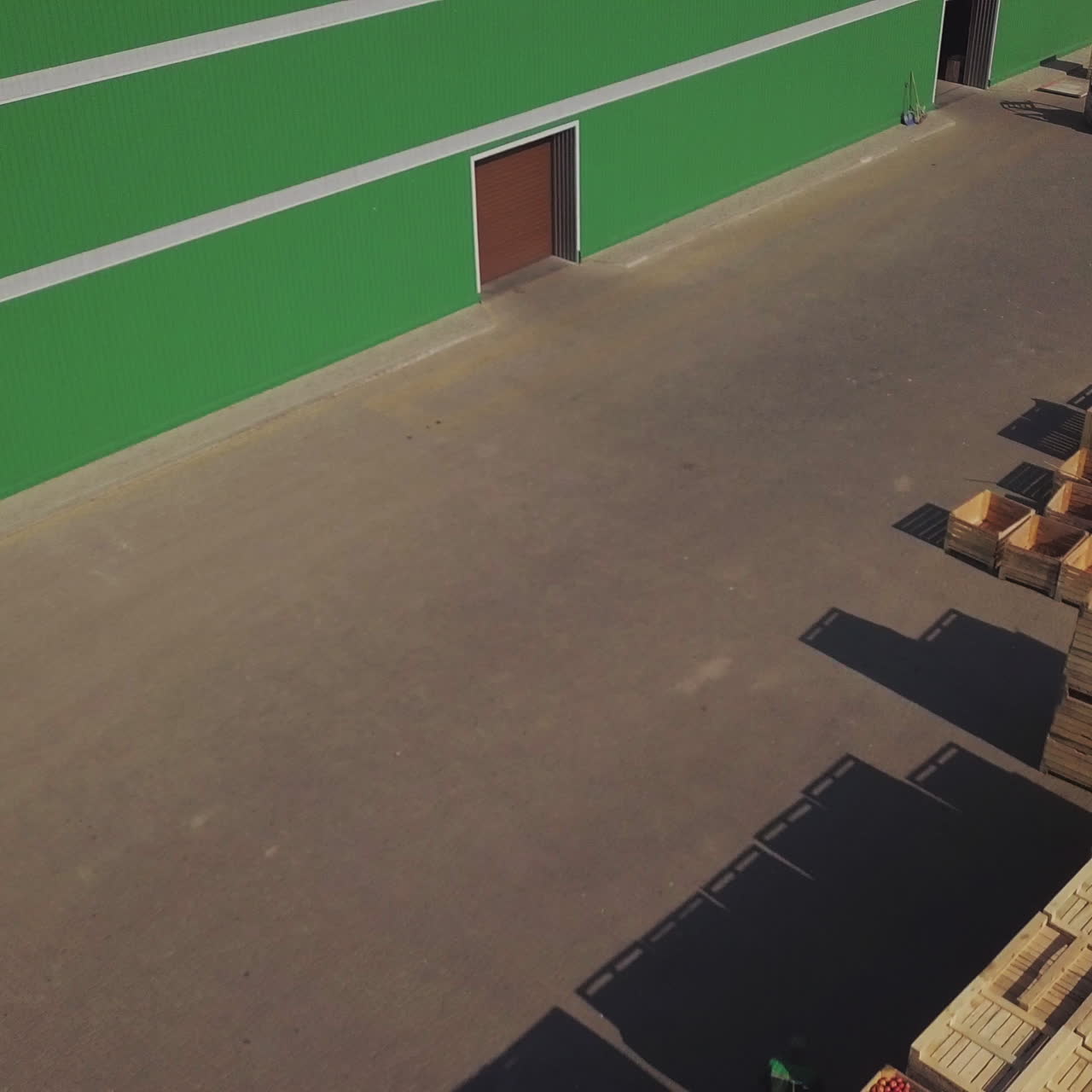 A small tractor is carrying a trailer with apples to the warehouse on the background of empty wooden boxes. Fruit processing plant.