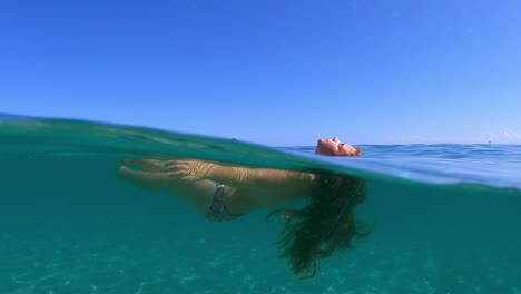 half underwater scene of little girl with long hair relaxing and floating in turquoise sea water