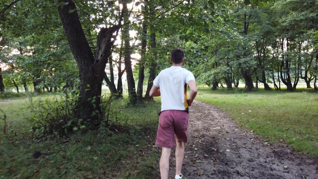 Giovane uomo caucasico che corre in un bosco su un sentiero d'estate.