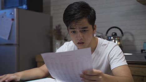 closeup view of a confused asian man calculating loan on computer at home is looking at the paper bill in shock upon finding out he can’t make the payment.