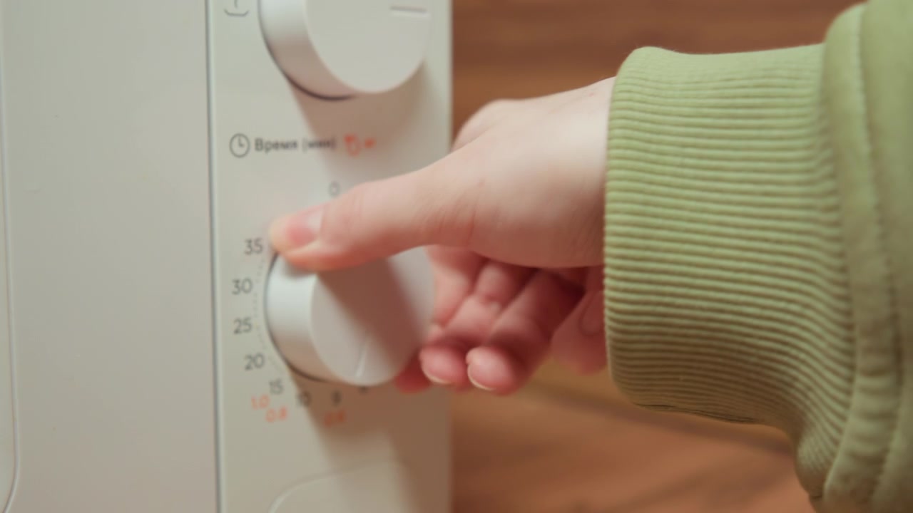 Close-up hand in green sleeve rotates large circular stitch selection dial on white sewing machine panel, changing numbered settings with careful precision inside warm craft workspace