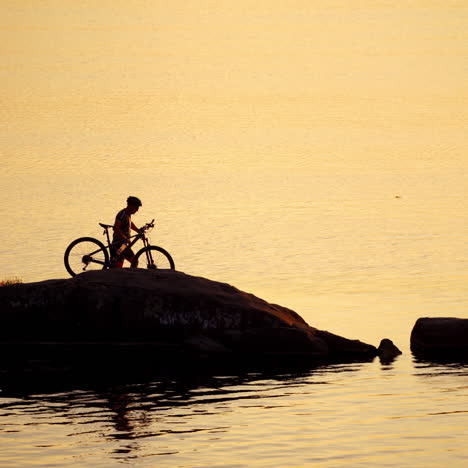 cyclist in helmet and glasses with his bike near the water. professional bicyclist comes to the river and washes his hands in water in the evening.